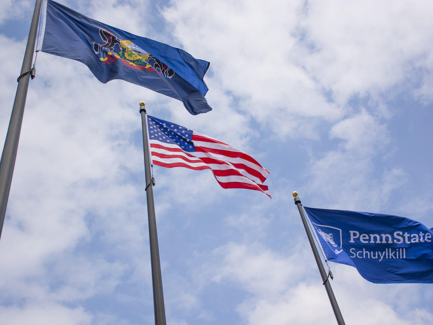Pennsylvania, U.S., and Penn State Schuylkill flags billow against a blue sky with bright white clouds