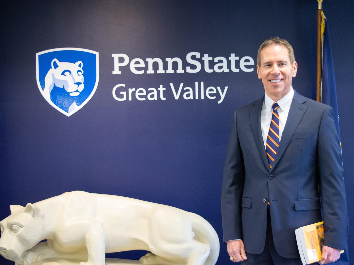 John J. Sosik standing in front of a nittany lion statue and a blue wall with the Penn State Great Valley logo