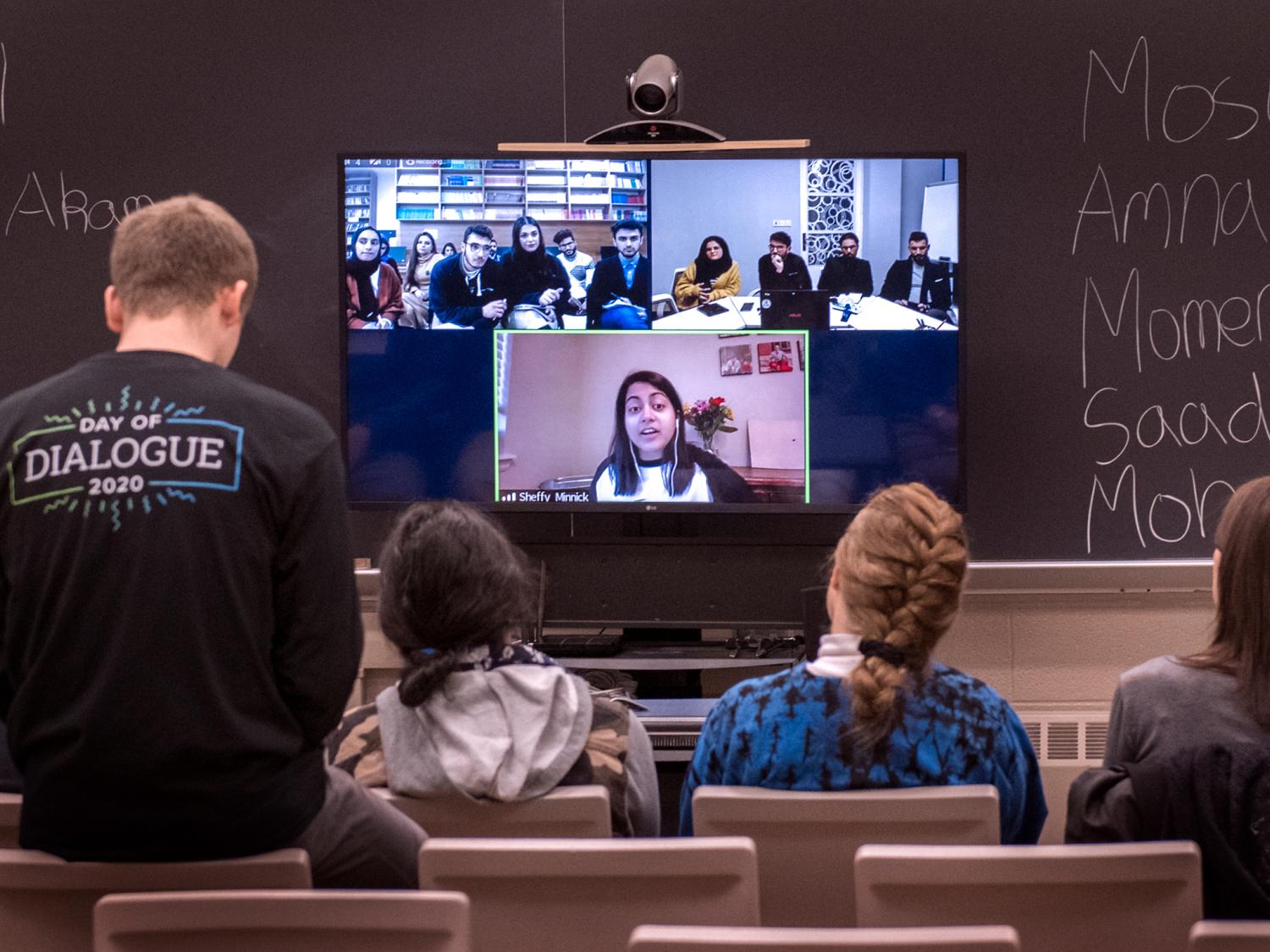 A group of people interacts with a woman who is speaking on a monitor
