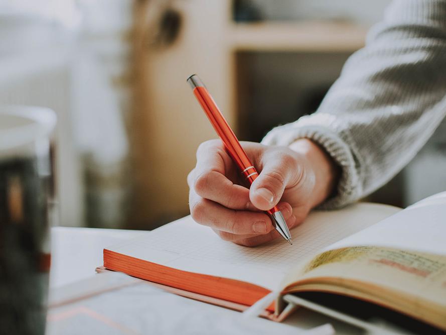 A hand holding a pen and writing in a book