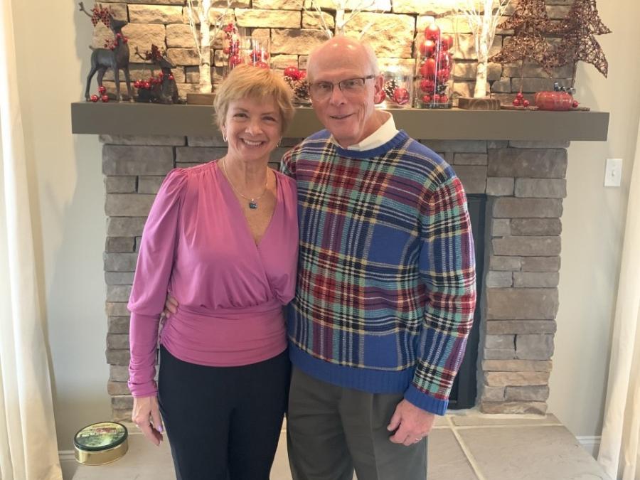 A woman and man stand in front of a fireplace and smile.