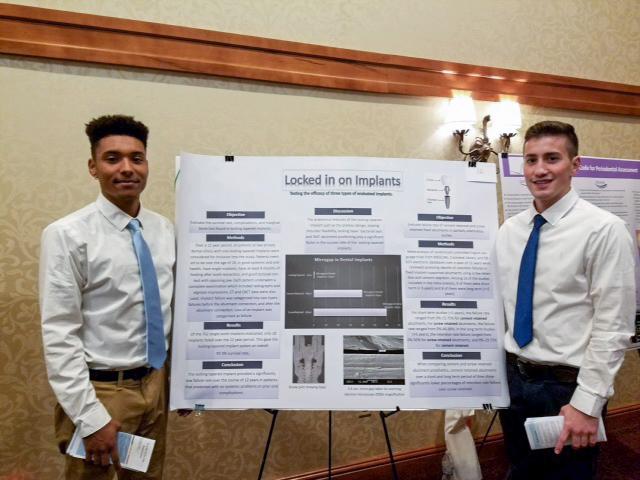 Two students stand with their poster presentation on dental implants
