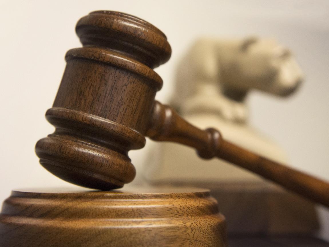 A gavel in the foreground, a replica of the Nittany Lion shrine in the background.