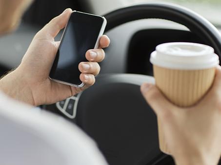 A driver holds a cup of coffee and a cell phone.