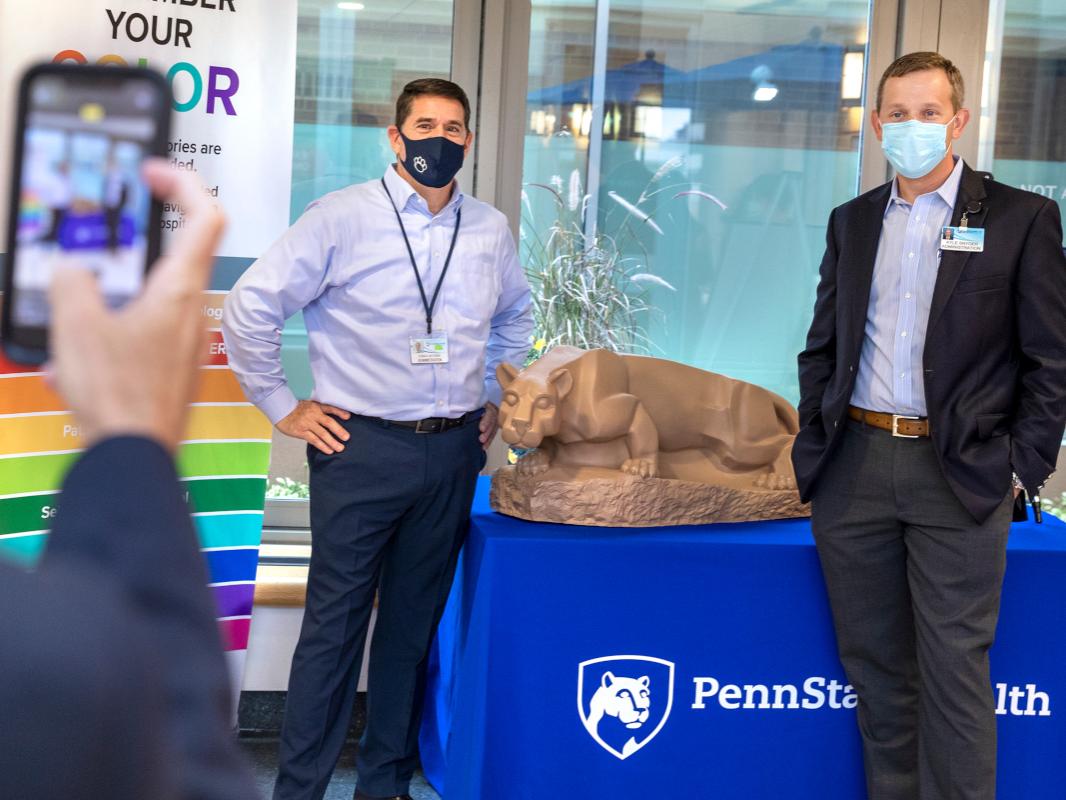 Two men pose for a photo in front of a statue of a lion