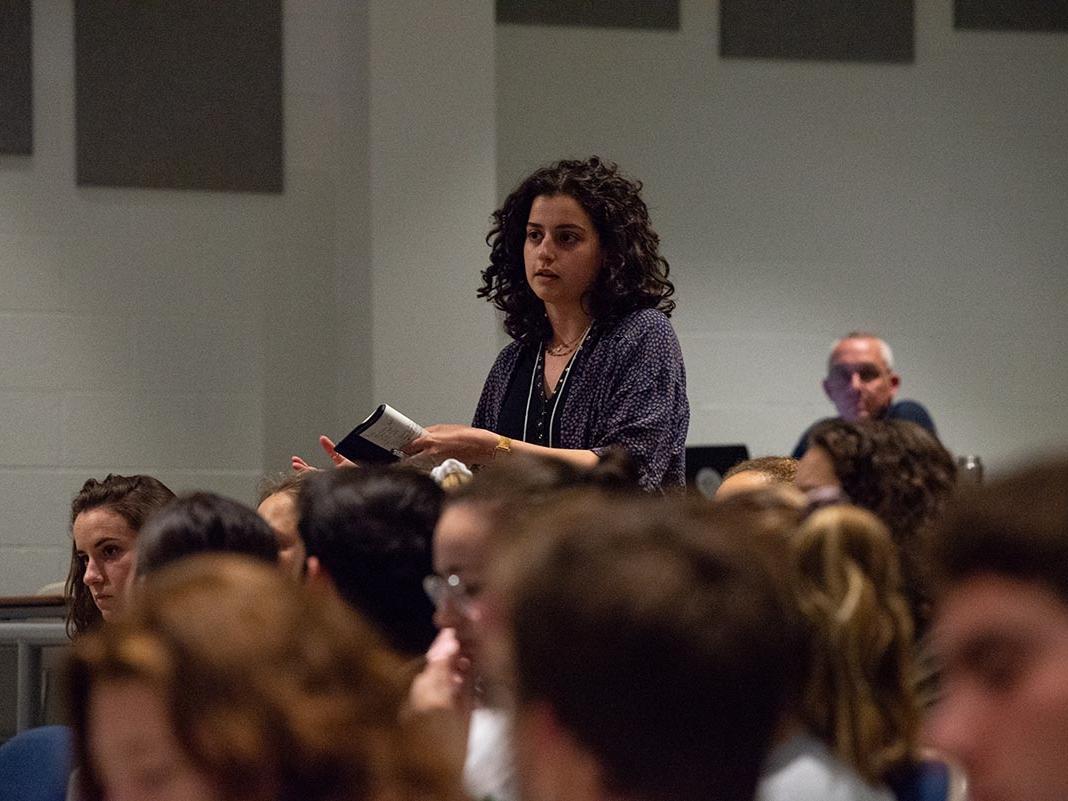 A woman stands to speak, surrounded by other students in an auditorium. 