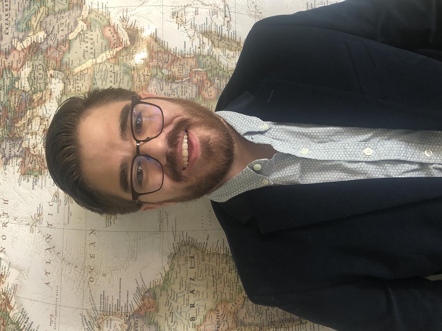 A student wearing glasses and a jacket smiles for a photo.