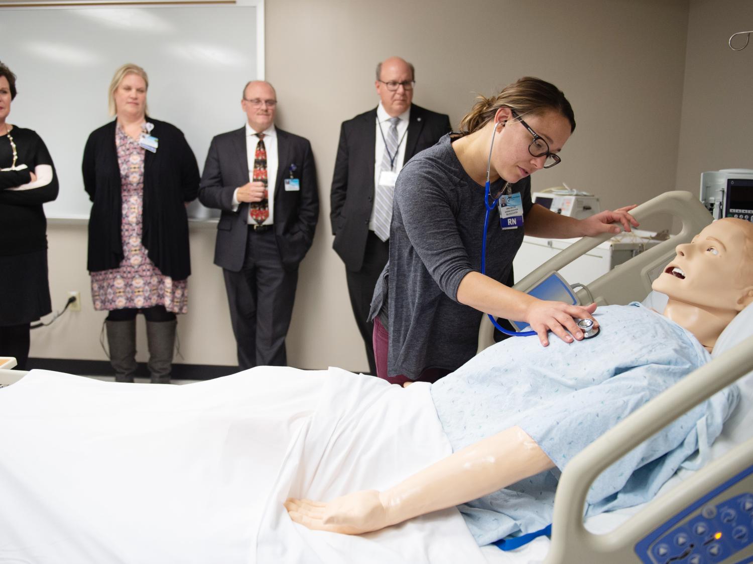 A nurse leans over a mannequin to demonstrate a medical technique
