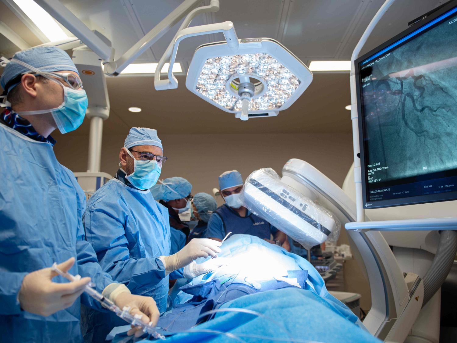 Four physicians dressed in scrubs perform a cardiac catherization.