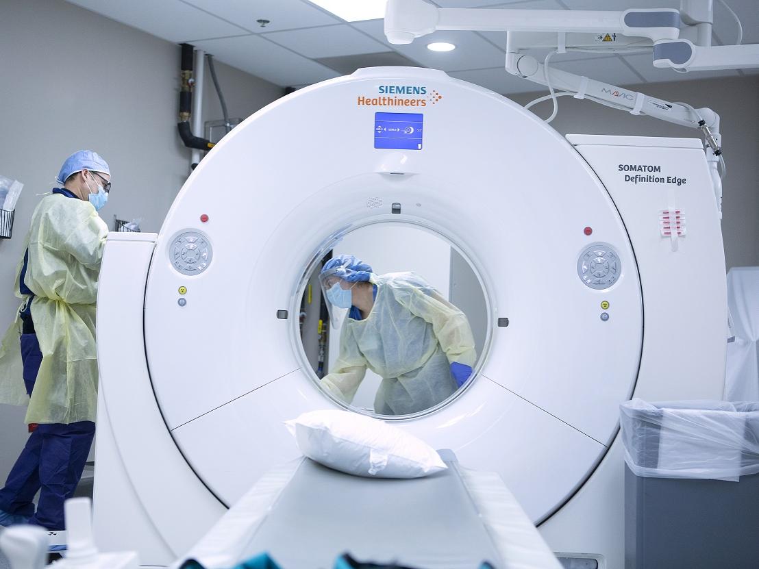 A man and woman wearing face masks, gloves and disposable body and head covers sanitize a CT scan room after use by a COVID-19 patient at St. Joseph Medical Center.