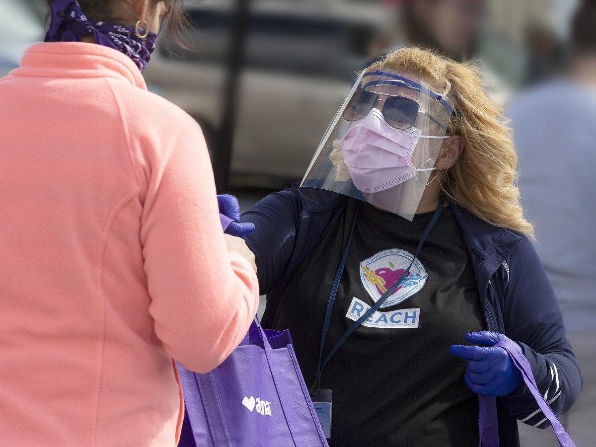 Madeline Bermudez, wearing mask, face shield and sunglasses, hands a bag to a woman wearing a mask.