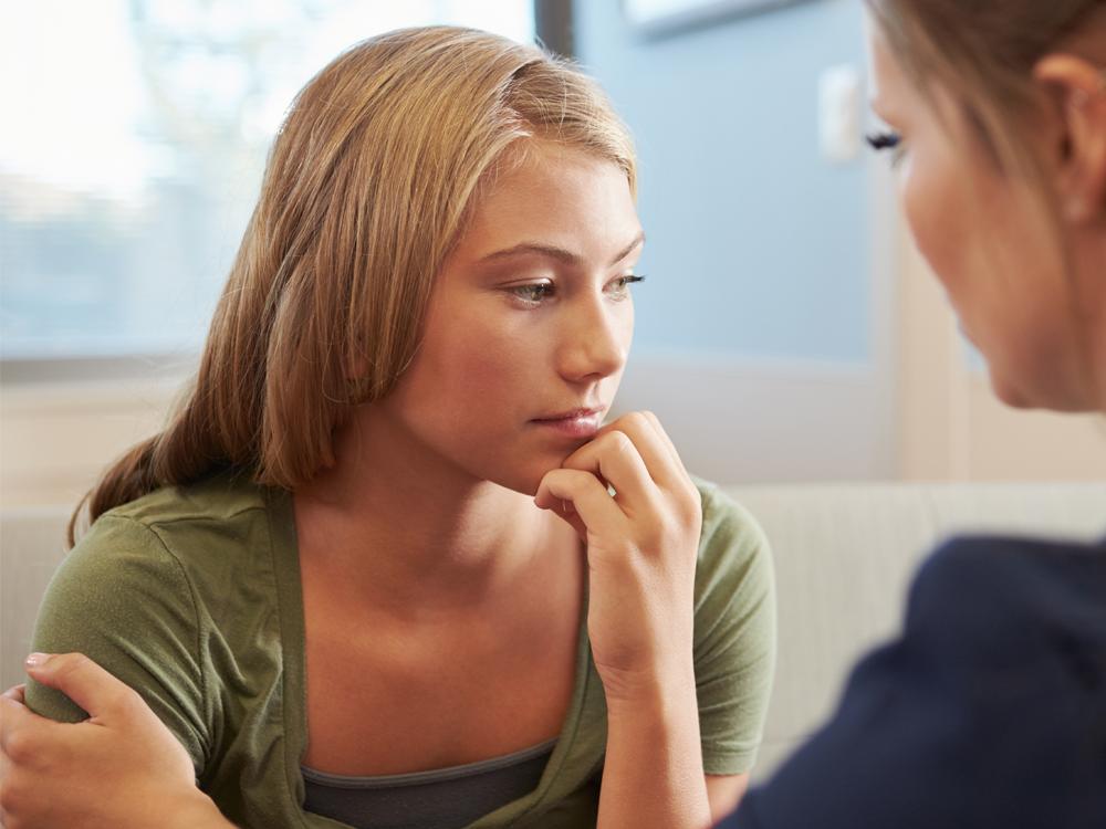 A woman talks with a teenage girl. Her hand is on the girl’s shoulder.