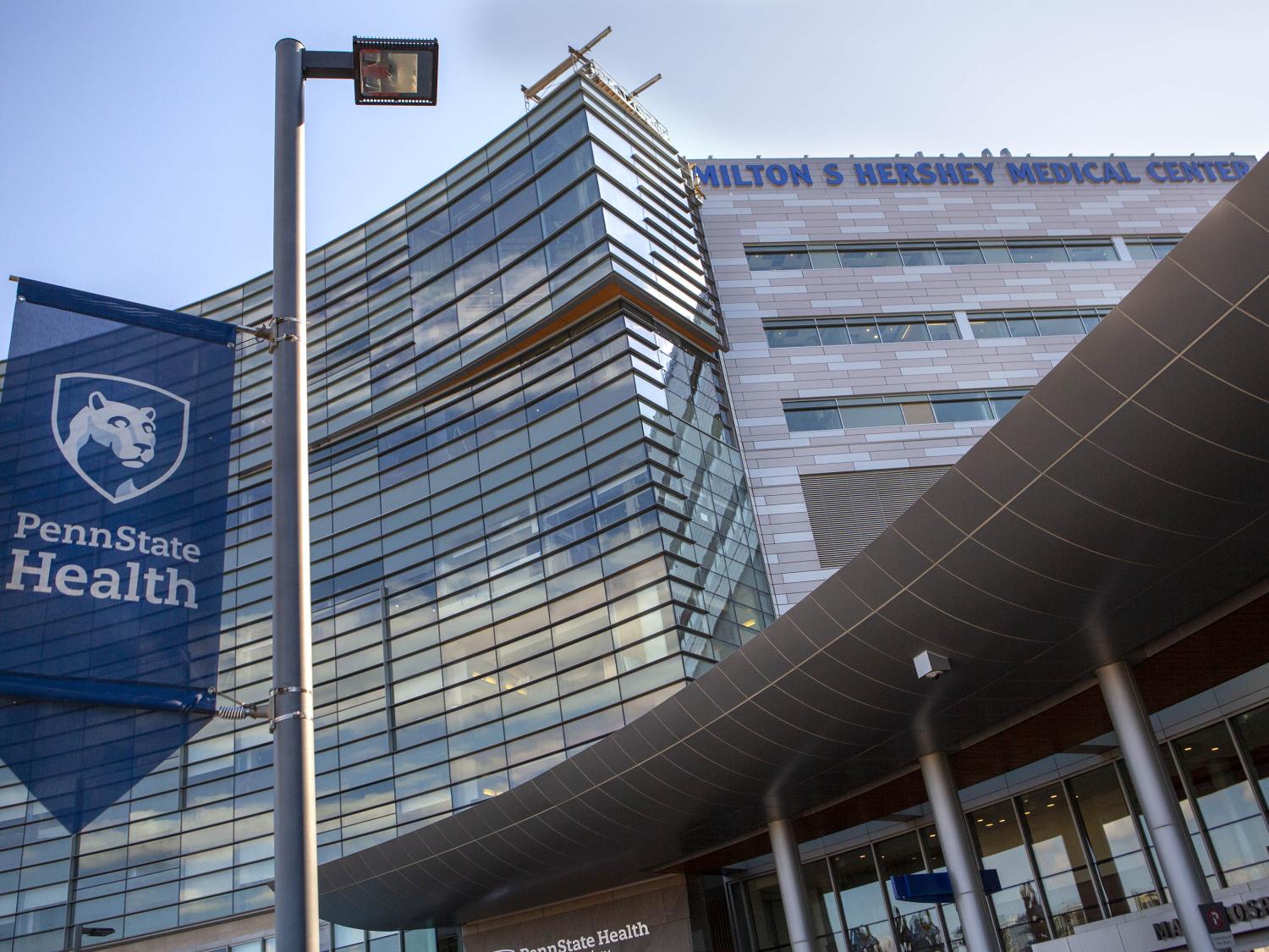 A view from the ground near the main entrance of Hershey Medical Center. A Penn State Health banner is in the foreground; the building is behind it.