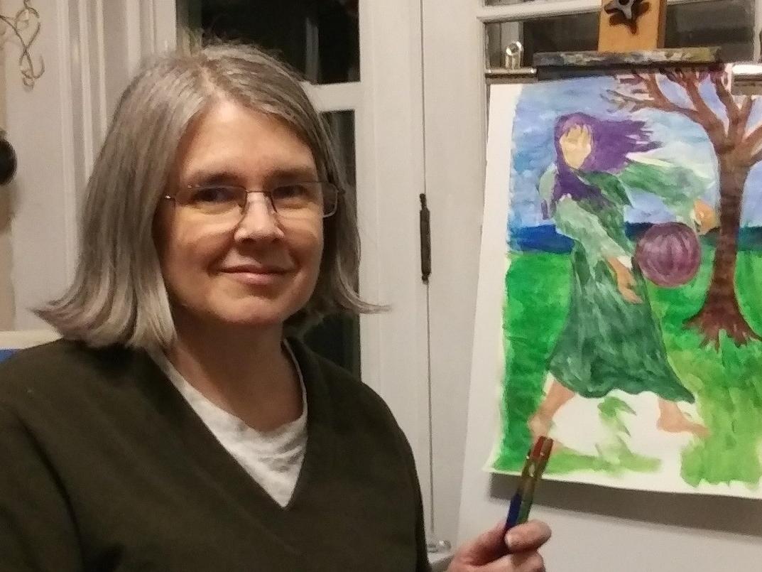 Jennifer Rudolph, who wears glasses and a V-neck sweater, sits at an easel and holds a brush in her hand. A painting on the easel shows a girl standing by a tree with her hair blowing in the wind.