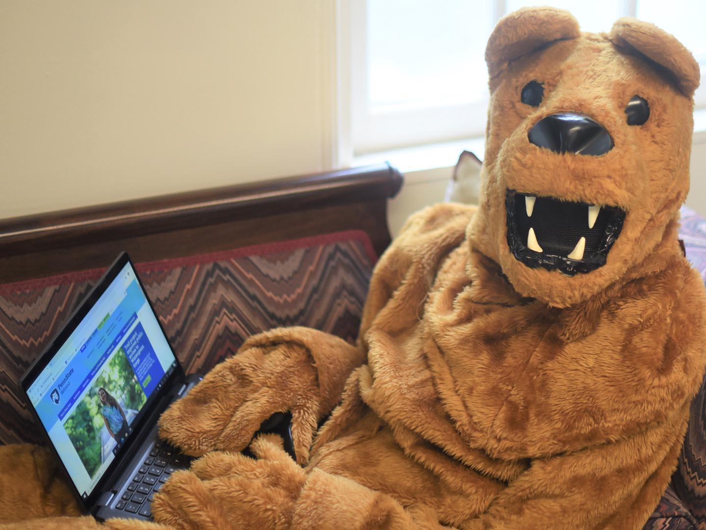 The Nittany Lion uses a laptop while reclining on a couch at Penn State Behrend.