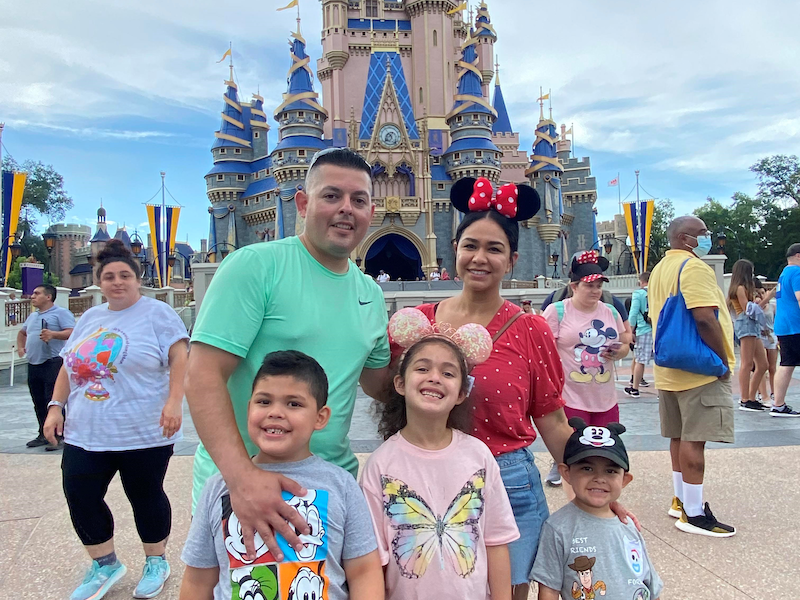 Husband, wife and three children pose for a photo in front of castle in Disney World's Magic Kingdom