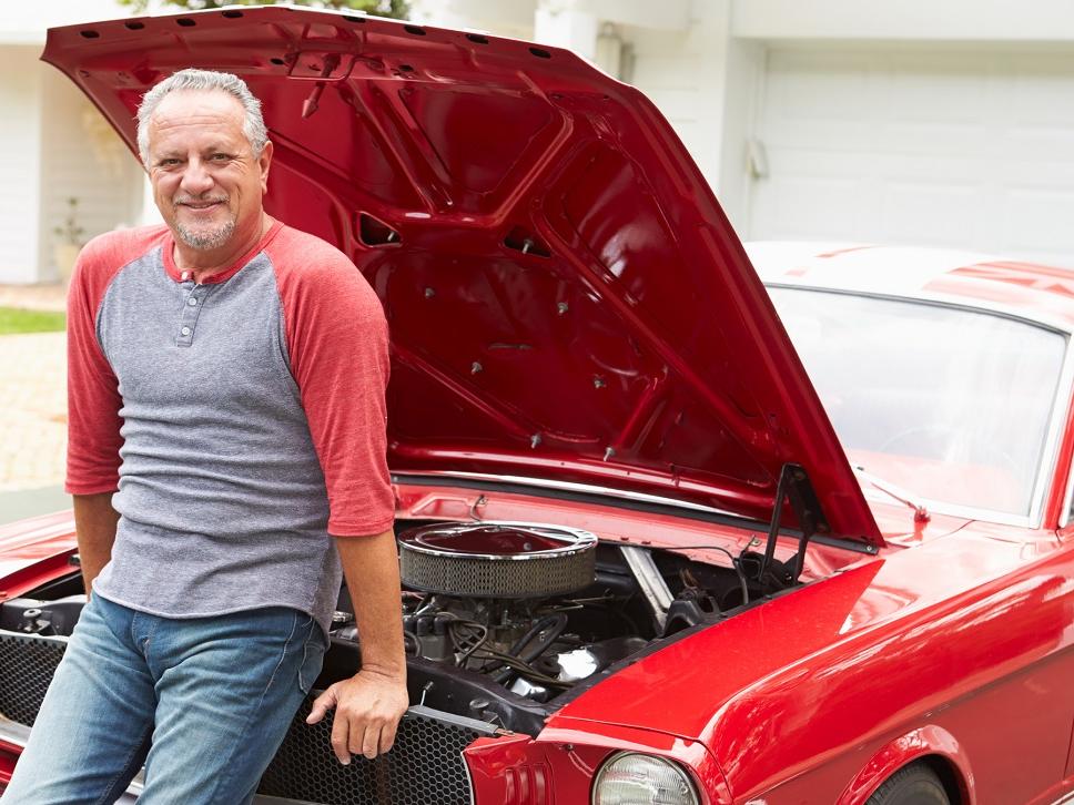 Retired senior man sitting on front of restored classic car.
