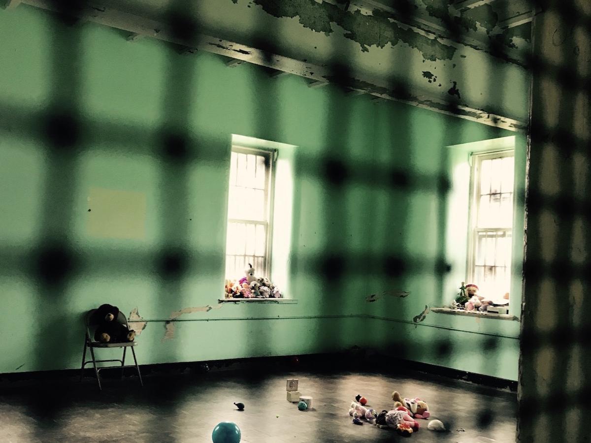 View, through caged door, of a nearly empty room in a former mental hospital.