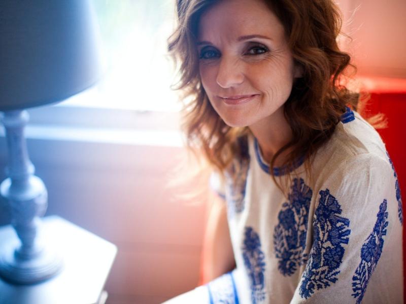 Singer-songwriter Patty Griffin sits in front of a window and smiles for the camera.