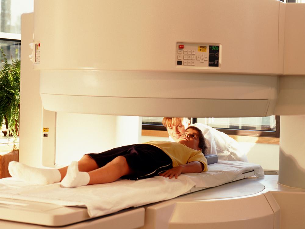A child lays on a medical imaging table; a medical professional is closeby.