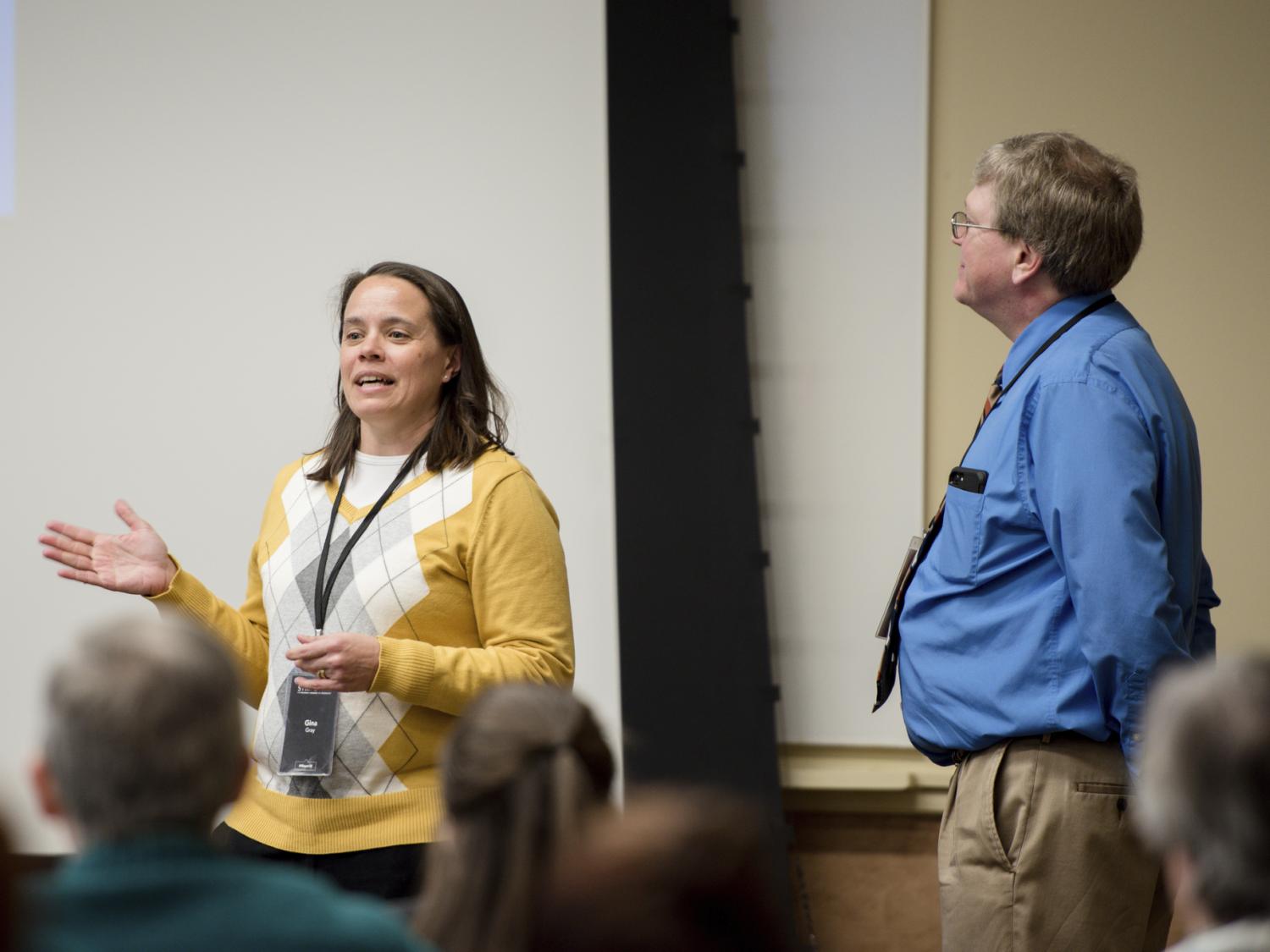 Gina talks while Griff listens and looks toward presentation screen