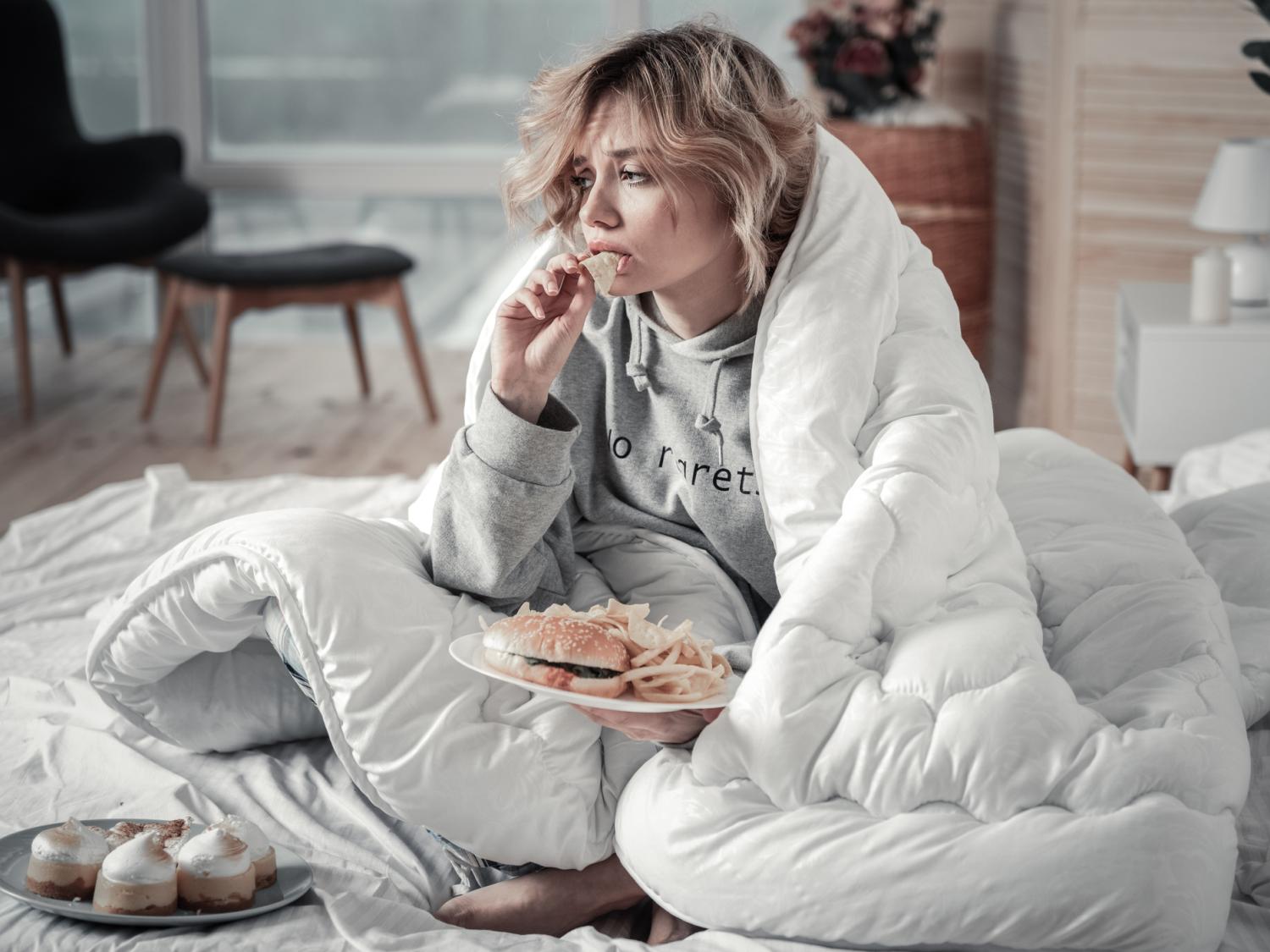 A woman eating ice cream looking sad and wrapped up in a blanket