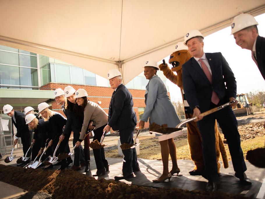 twelve people with shovels in hand turn over dirt