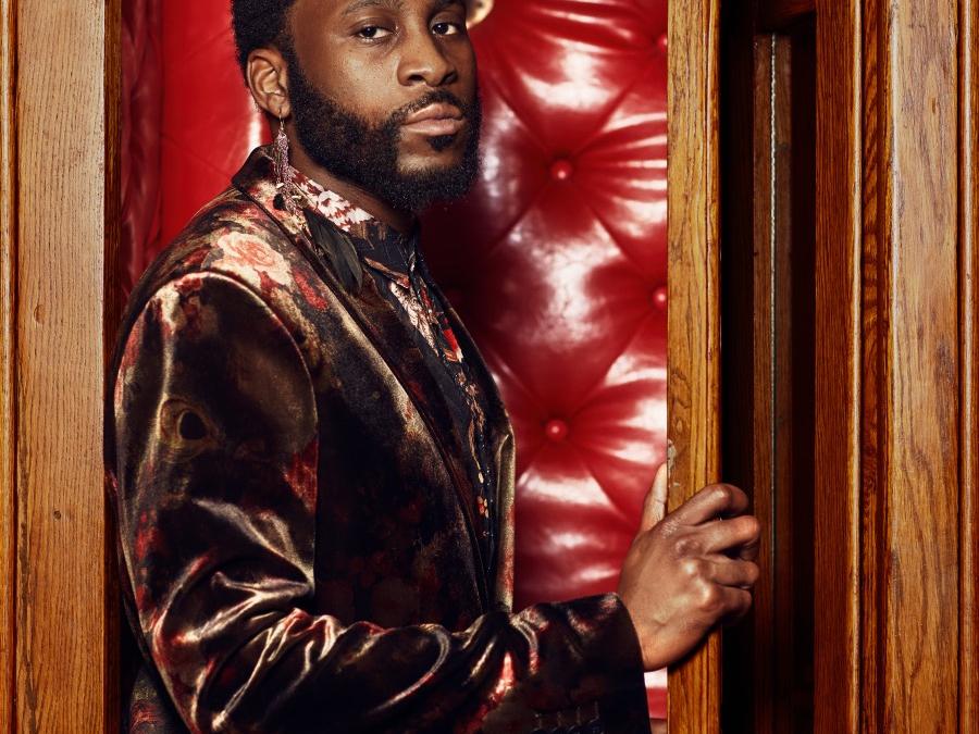 A man wearing a suit stands inside a wooden booth.
