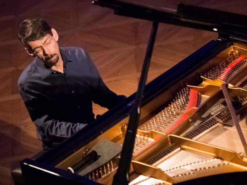 Fred Hersch sits and plays a piano with his eyes closed and lips pursed.