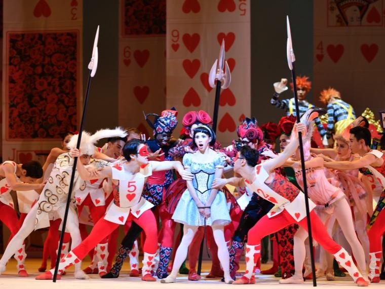 A dancer resembling Alice is surrounded by dancers dressed as playing cards and flamingoes.