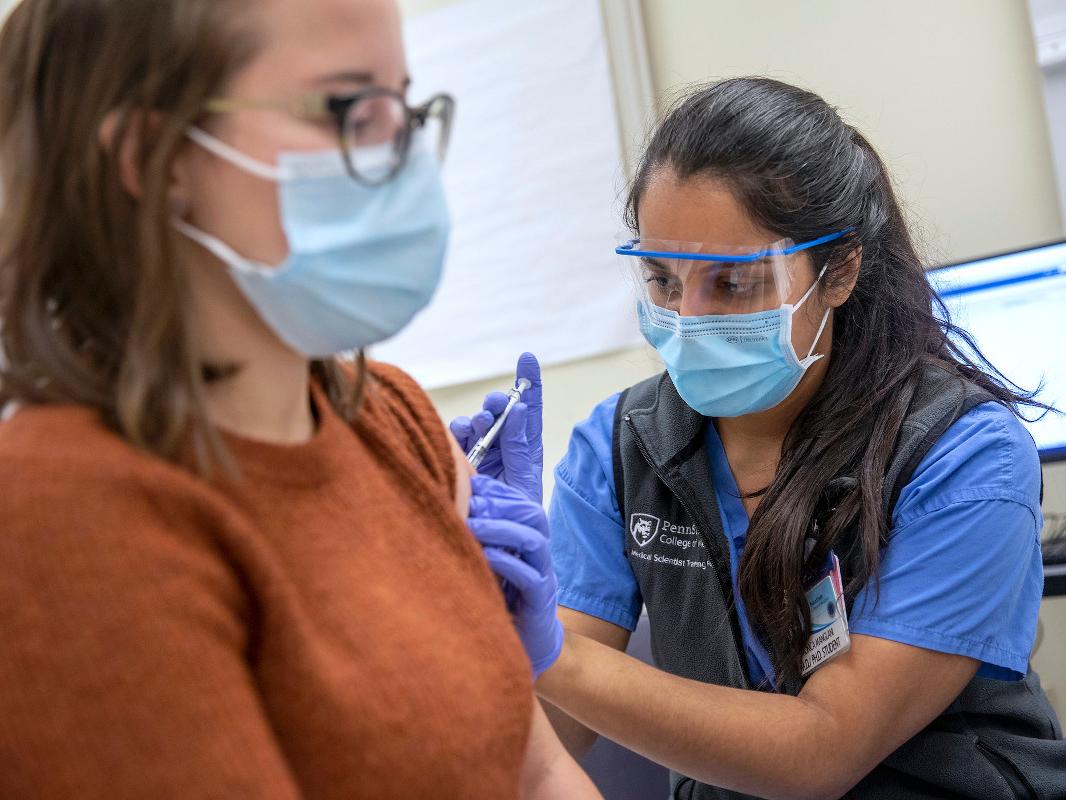 A woman wearing personal protective equipment give another woman a vaccine
