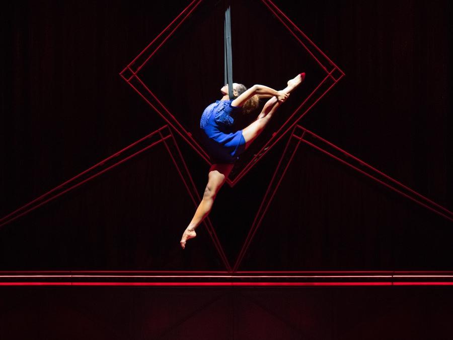 An acrobat hangs from suspended ropes above a dimly lit stage.