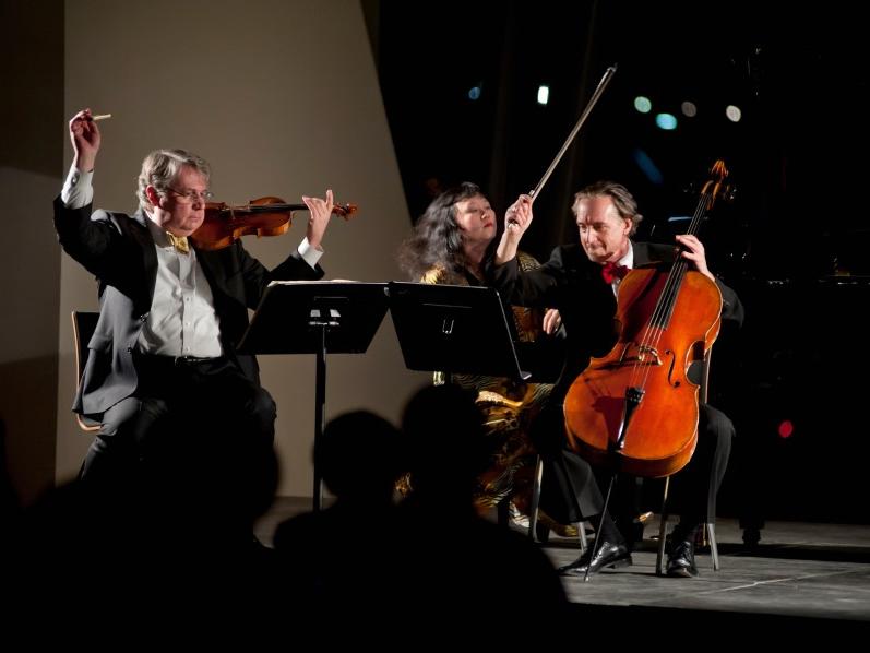 Violinist Philip Setzer, pianist Wu Han, and cellist David Finckel sit at music stands and play their instruments.