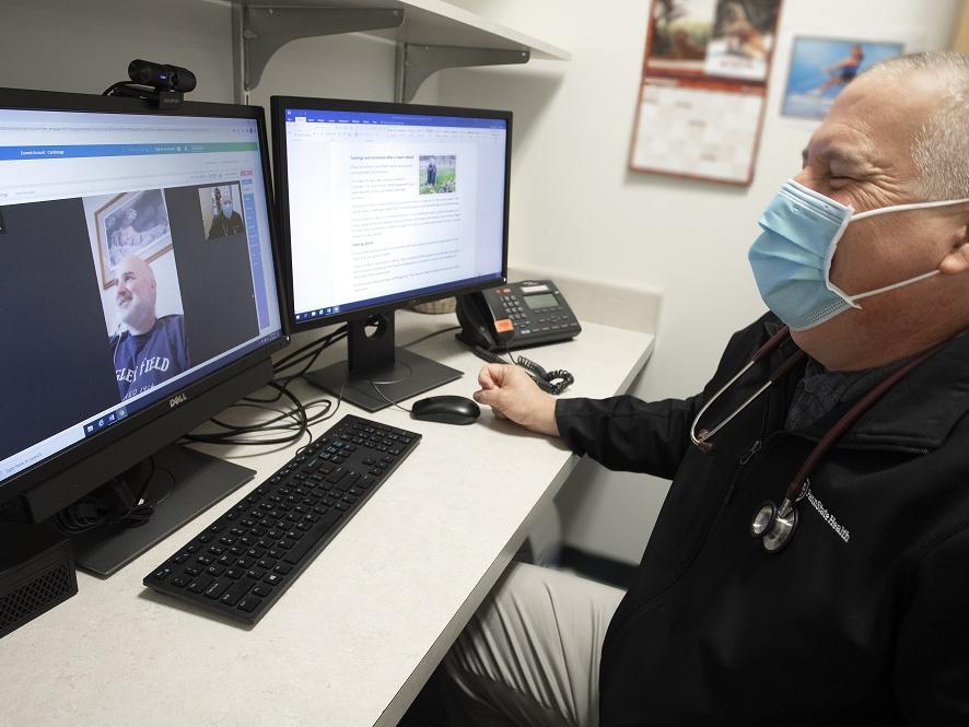 Exercise physiologist Mike Zehner laughs while conducting a virtual cardiac rehabilitation visit on a computer screen with patient Brian Welsh.