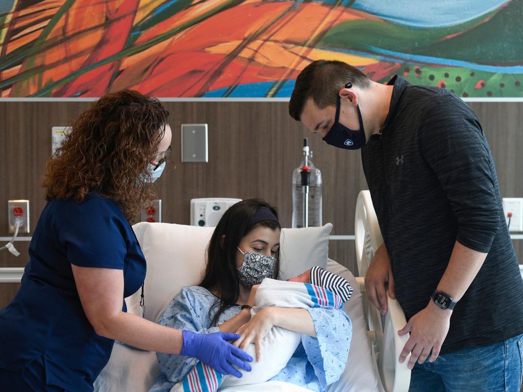 Two parents look at their newborn while a nurse looks on