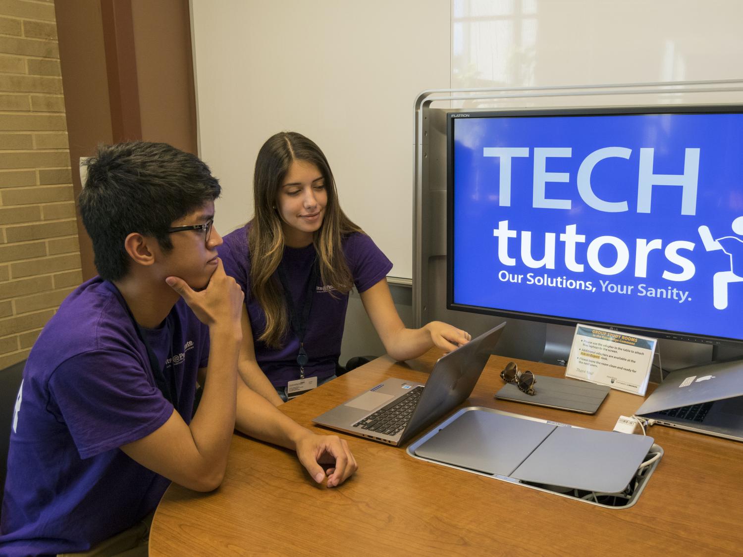 A male and female student look at a computer while sitting at a round table