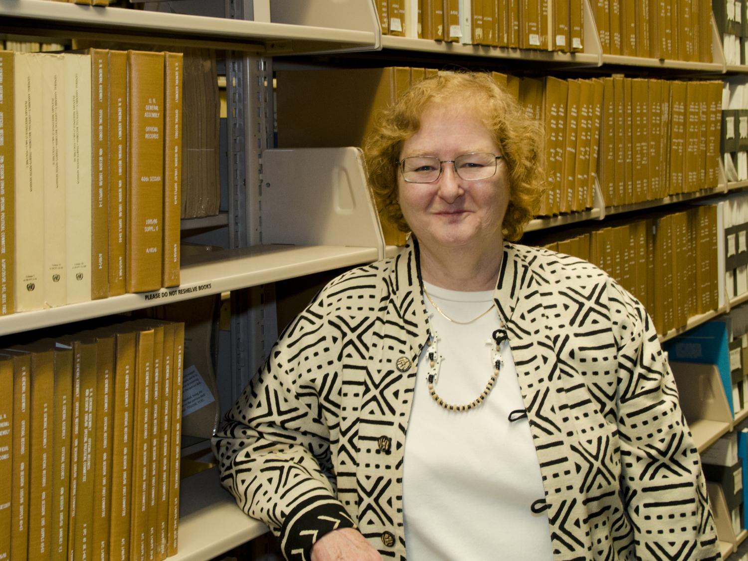 horizontal portrait of Helen Sheehy standing in front of shelves of bound government documents