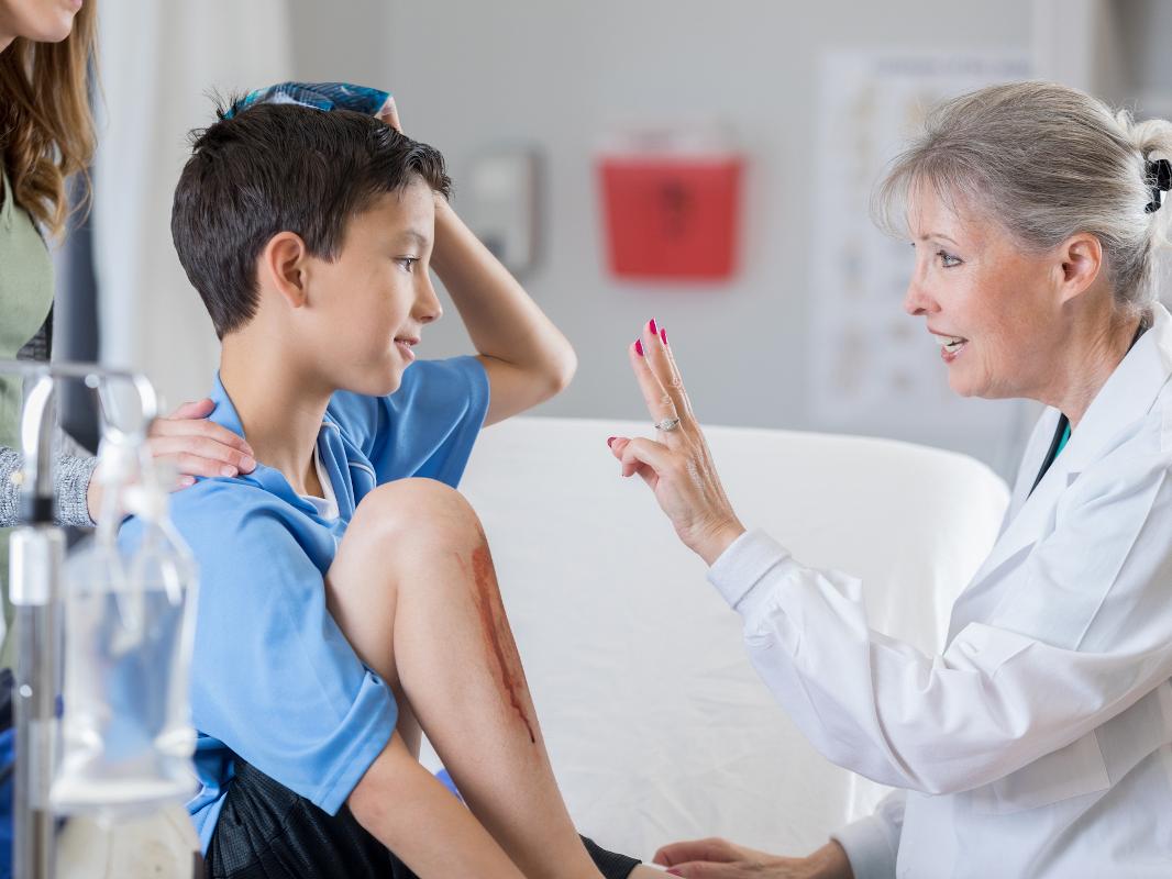 A physician performs a visual assessment of a young patient holding an ice pack to their head. 