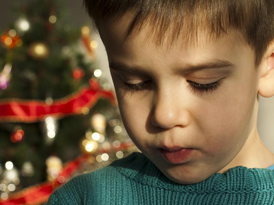 A boy looks down, with a Christmas tree in the background.