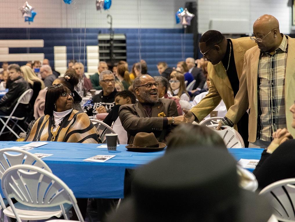 Men shake hands among guests sitting at table