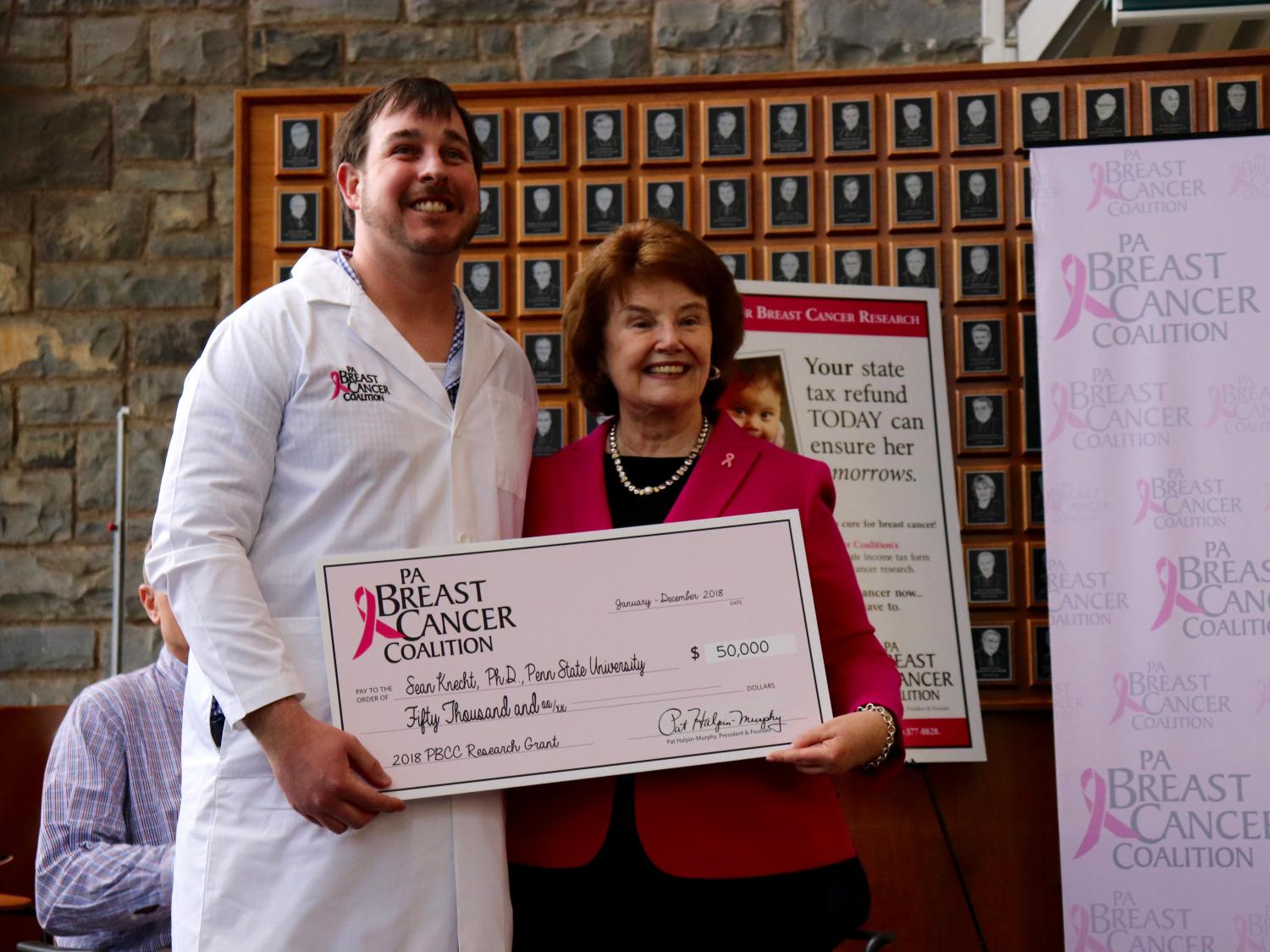 Sean Knecht receives a large cardboard check from Pat Halphin-Murphy, the president and of the Pennsylvania Breast Cancer Coalition