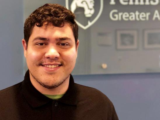 Student Derrick Ferrer smiling in front of Penn State Greater Allegheny logo 