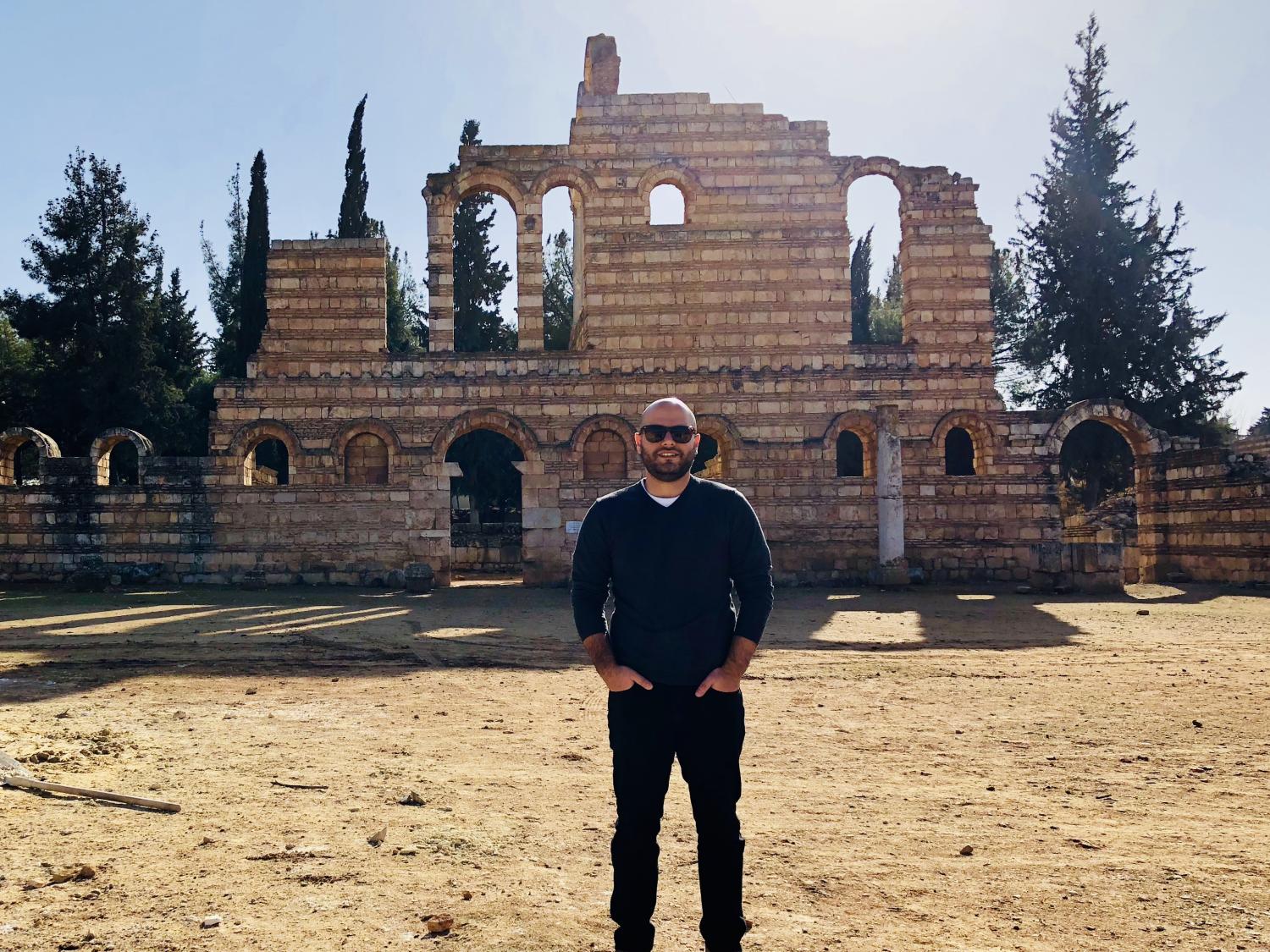 A Lebanese man stands in front of ruins. 