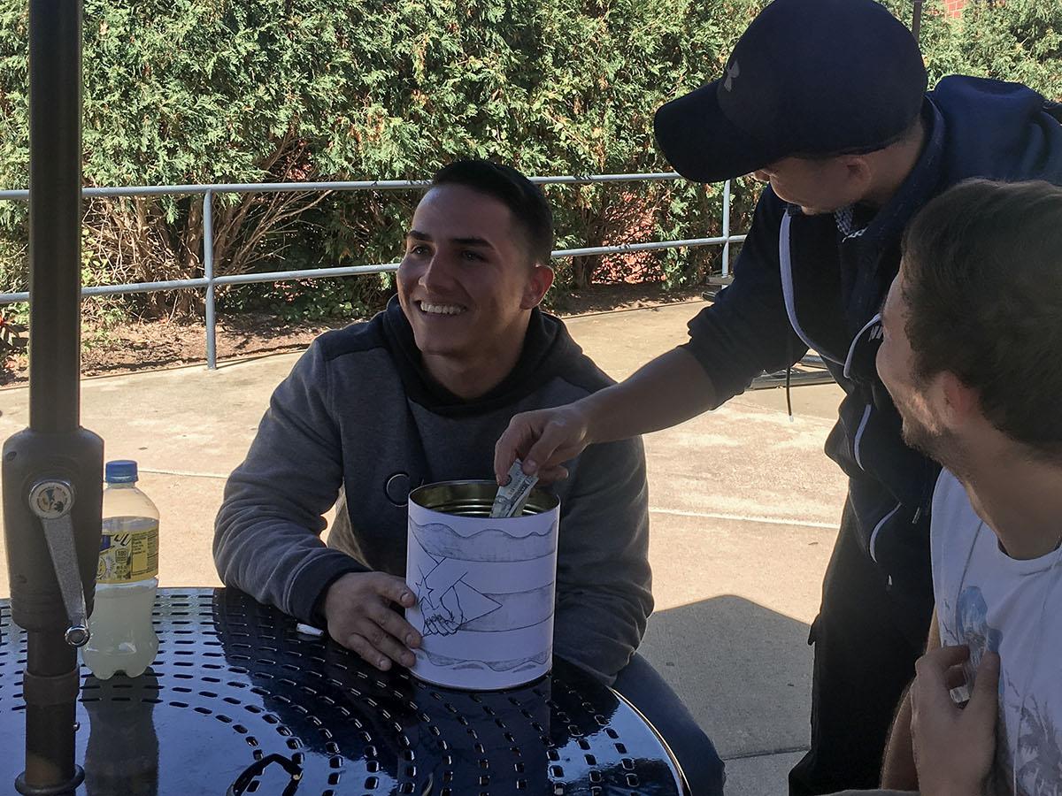 Students Pedro Escobar and Marcos Lopez collect a donation from Dash Phuyel in a can wrapped in a drawing of the Puerto Rican flag outside of Café Metro.  