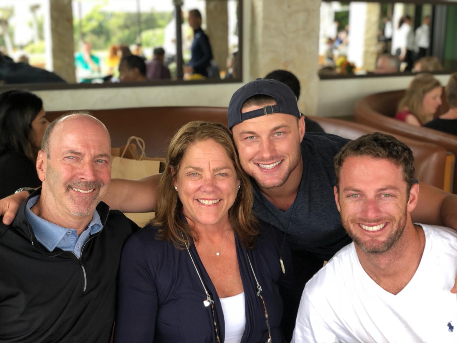 Three men and one woman pose and smile brightly while sitting closely together.