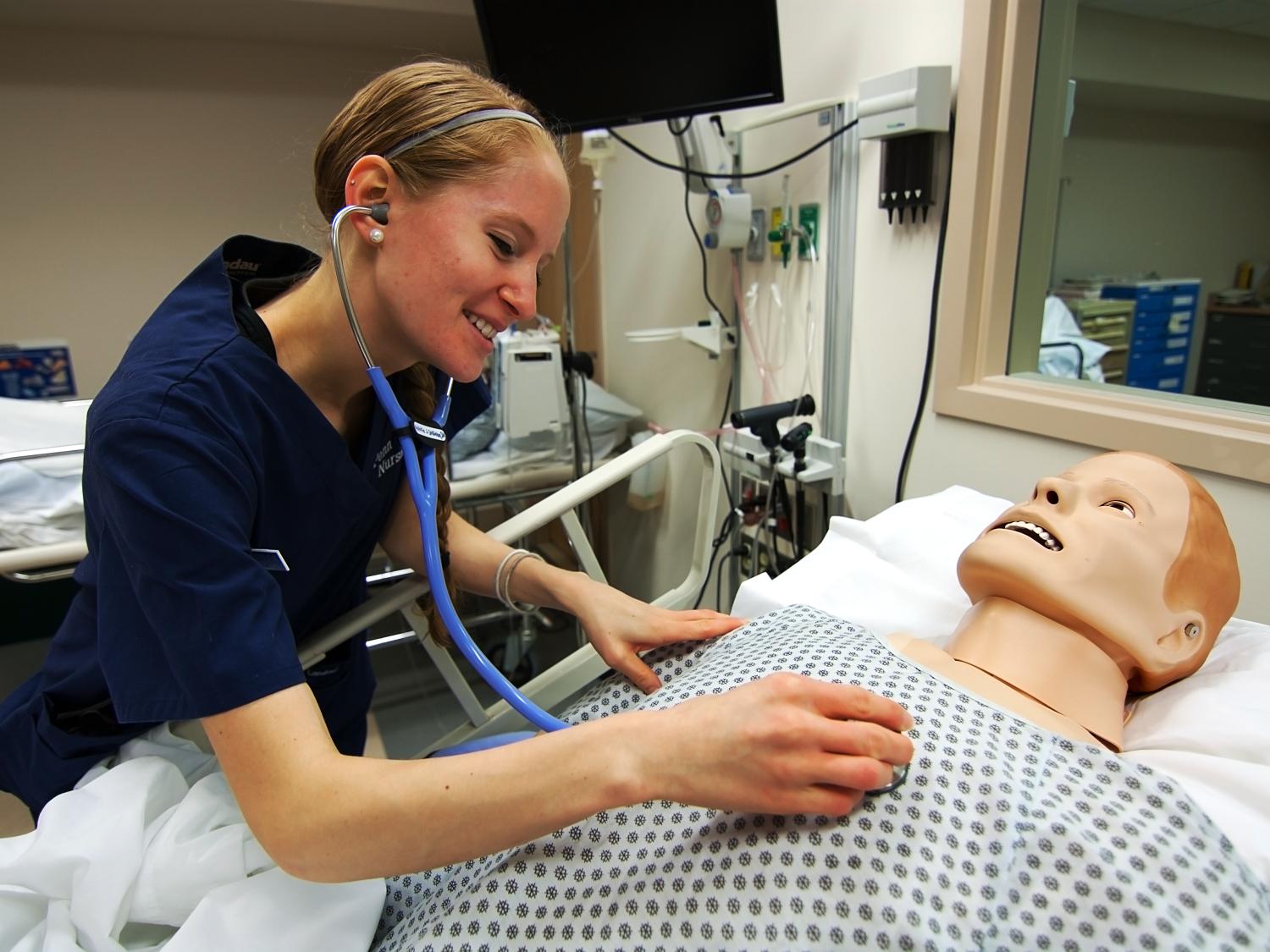 Natalie Sullivan uses a stethoscope to listen to a mannequin's heartbeat. 