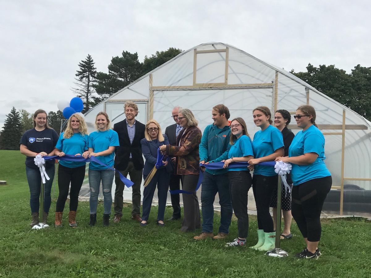 Beaver students and administators cut a ribbon in front of a high tunnel greenhouse.