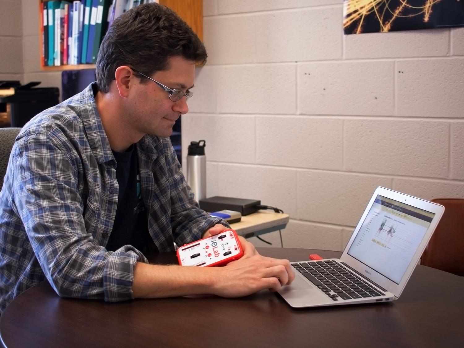 A man holds the iOLab device while staring at his computer.