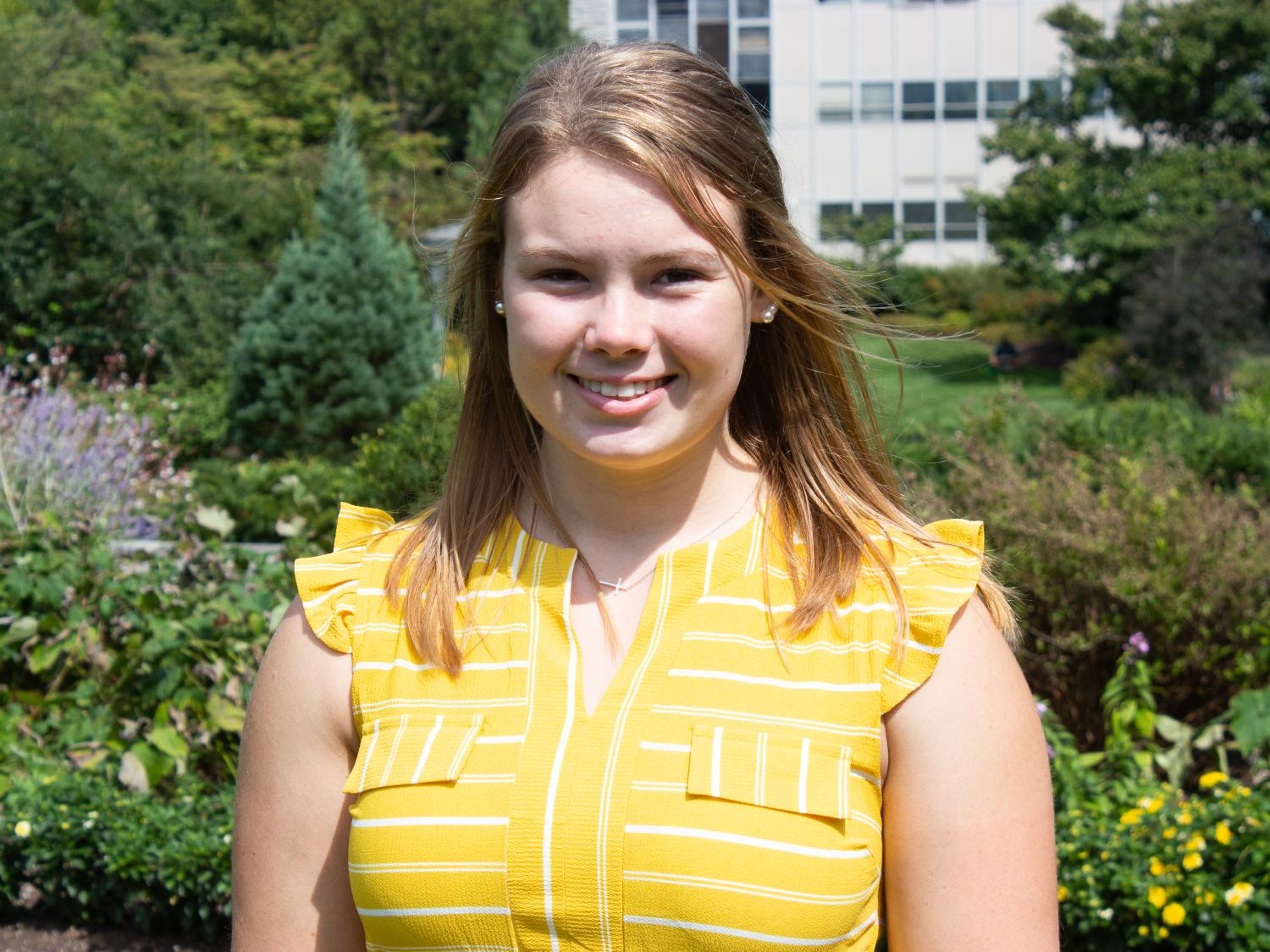 A blonde undergraduate female student smiles in a garden. 