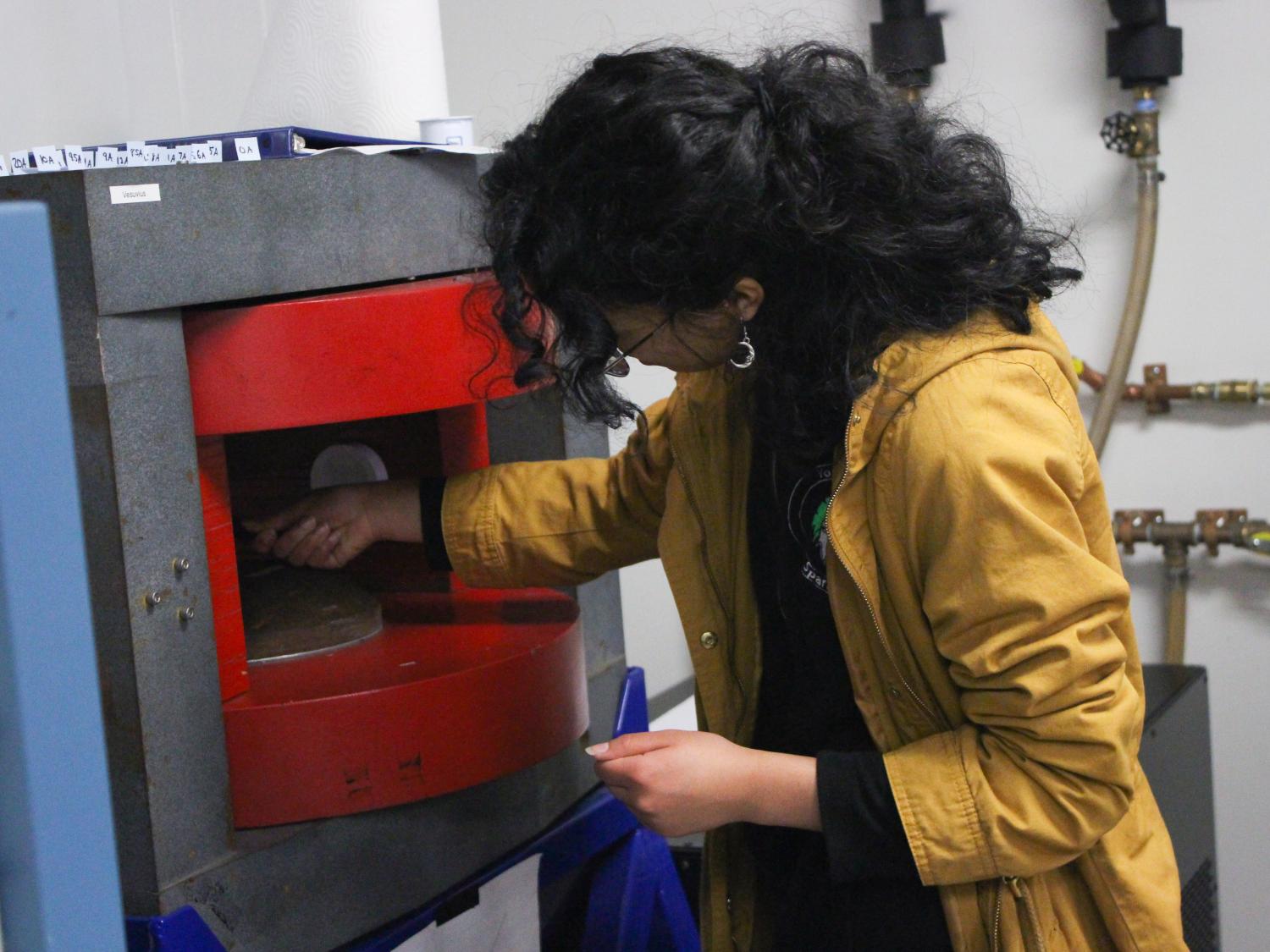 A female high school student works with a piece of machinery in a lab. 